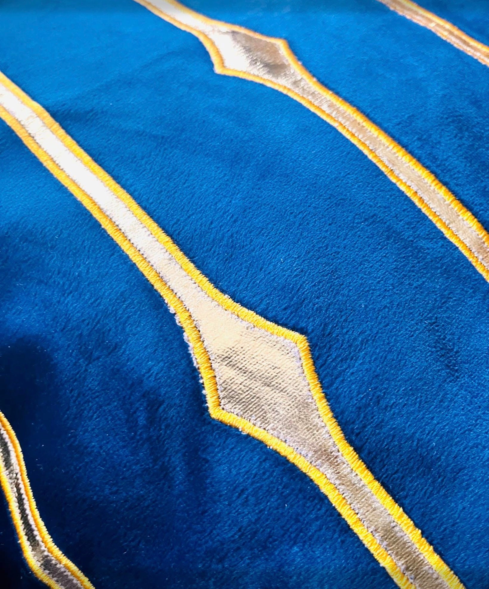 Close-up texture shot showing the bright blue velvet fabric and metallic gold diamond stripe appliqué detail.