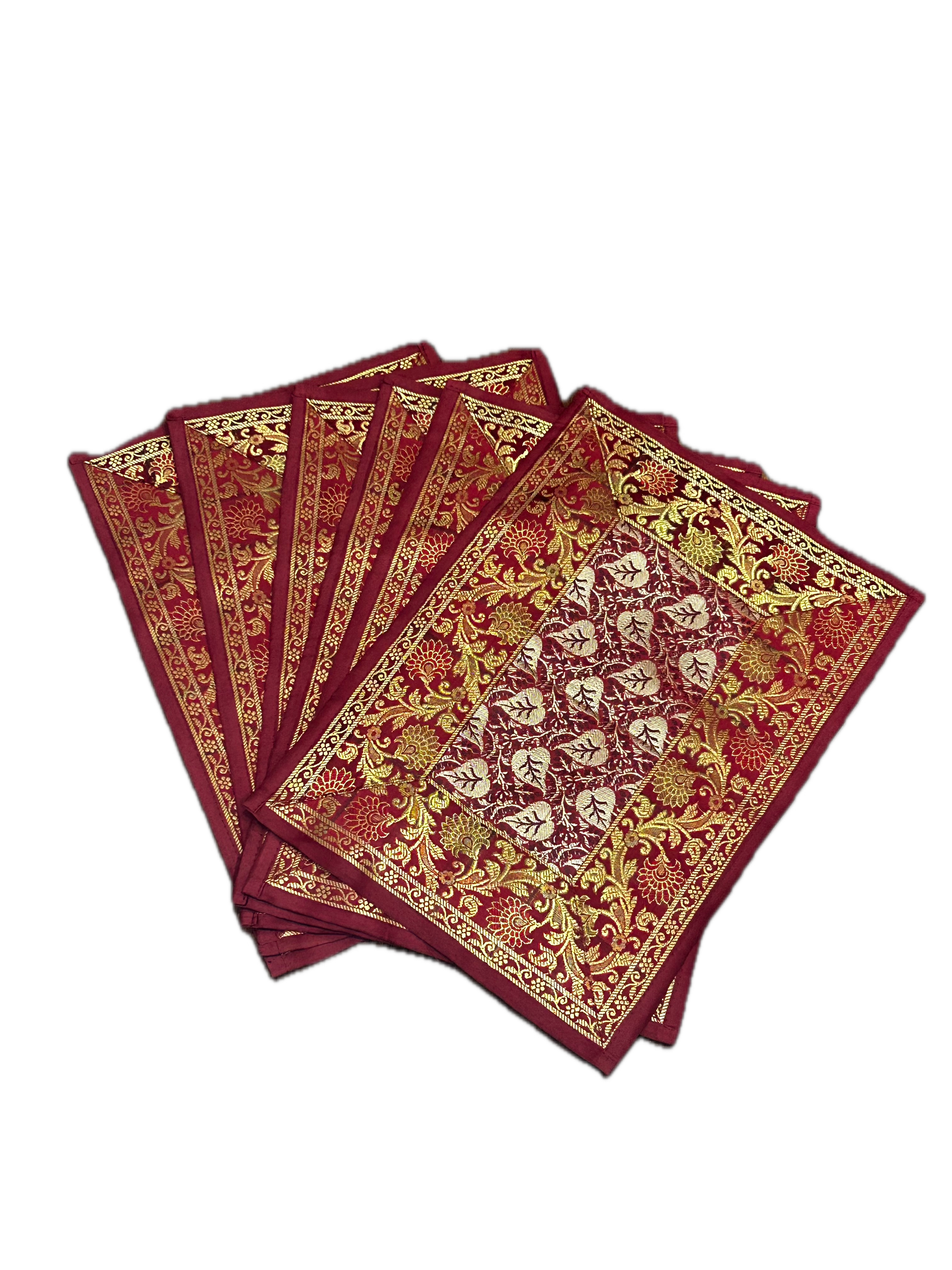 Fanned stack of six rectangular deep crimson placemats showing intricate gold and silver floral and leaf brocade motifs.
