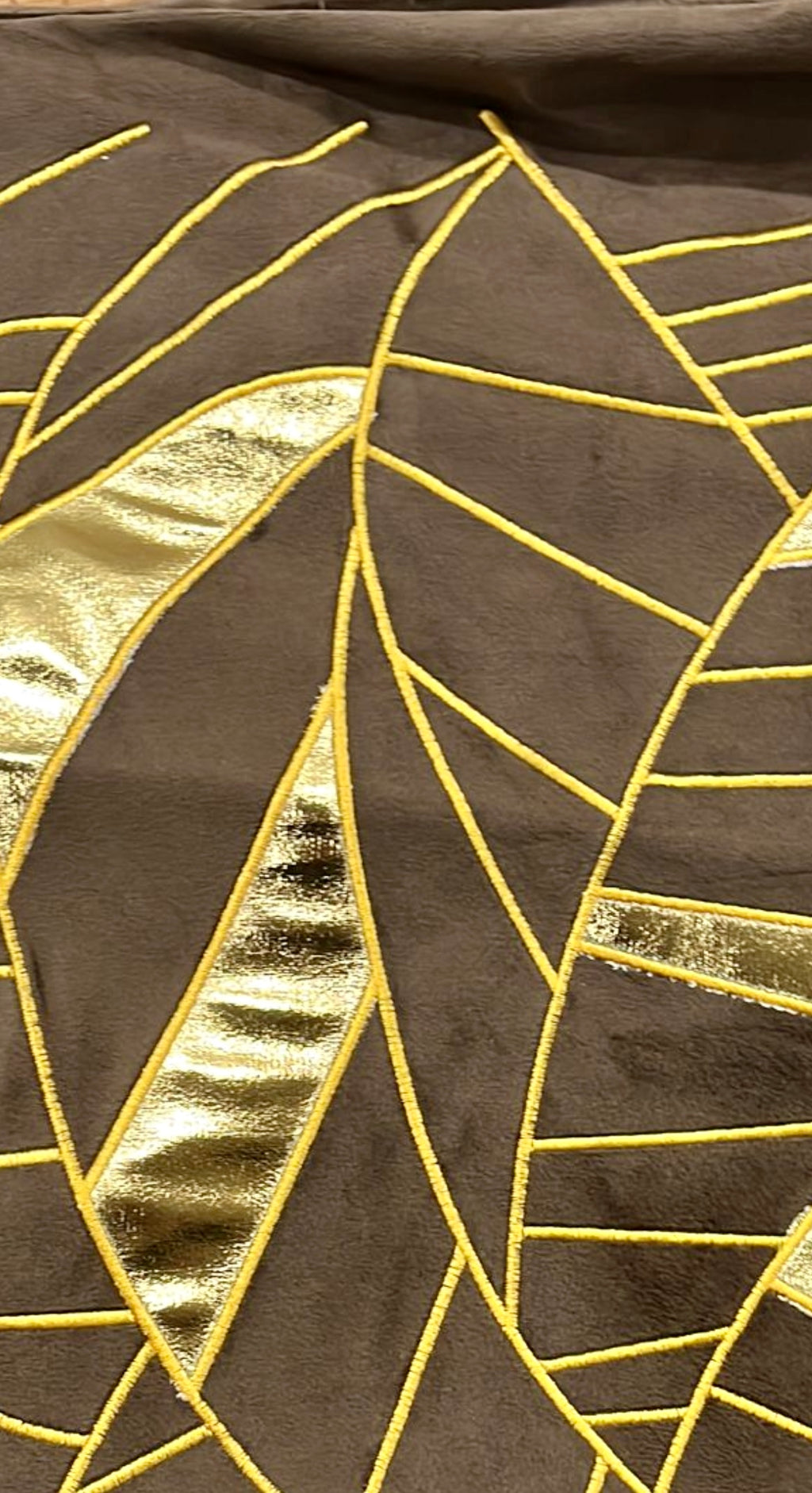 Close-up texture shot of a chocolate brown velvet cushion cover featuring intricate gold metallic leaf embroidery and geometric applique details.