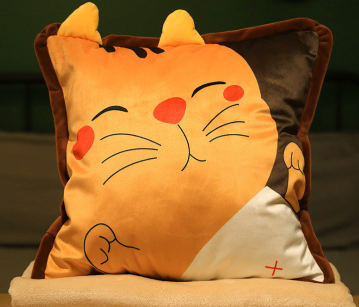 Orange plush pillow featuring a happy sleeping cat face with 3D ears, stacked on soft beige blankets.